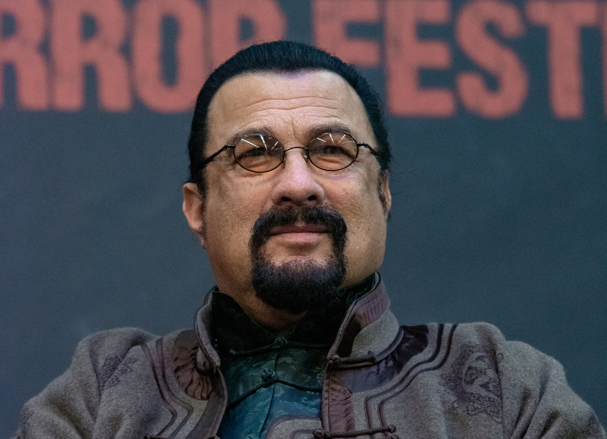 Steven Seagal wearing green jacket and glasses is smiling - 2018