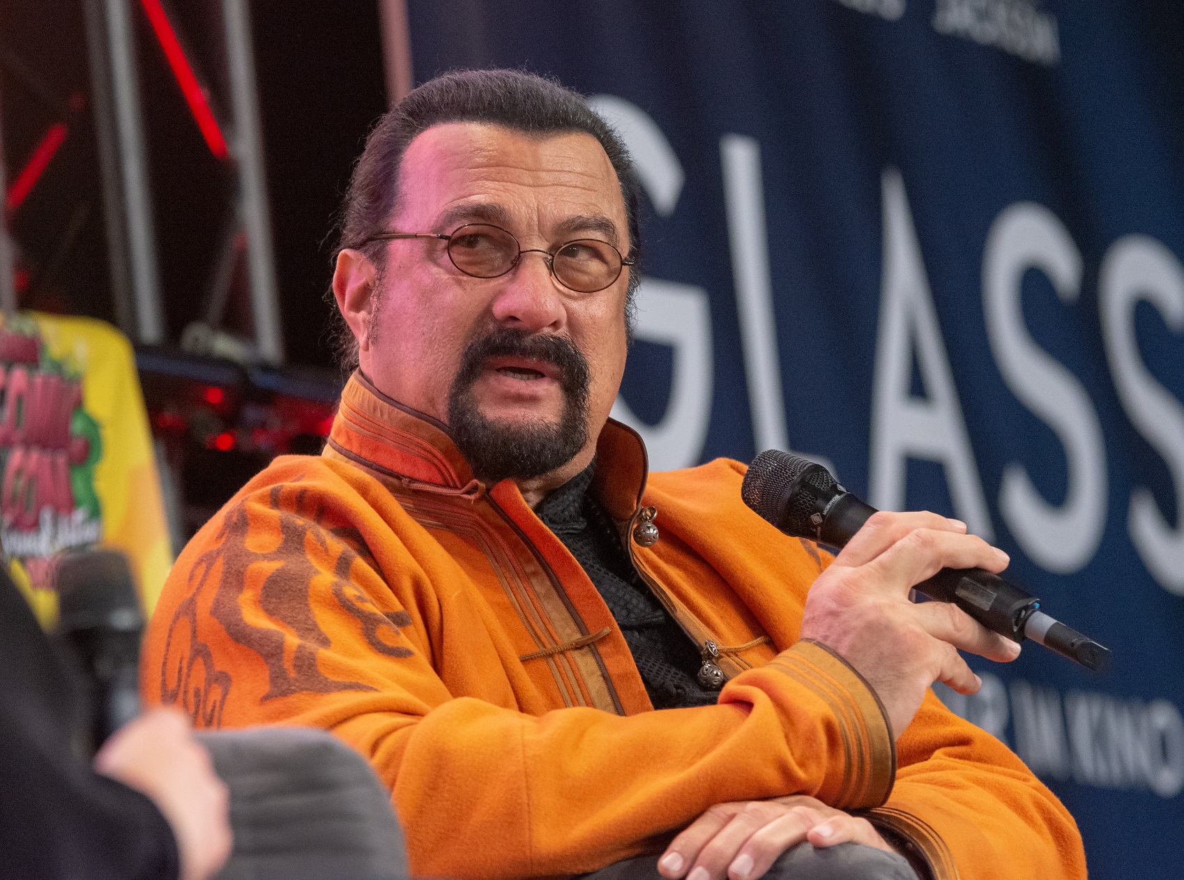 Steven Seagal wearing orange jacket and glasses is looking at side - 2018