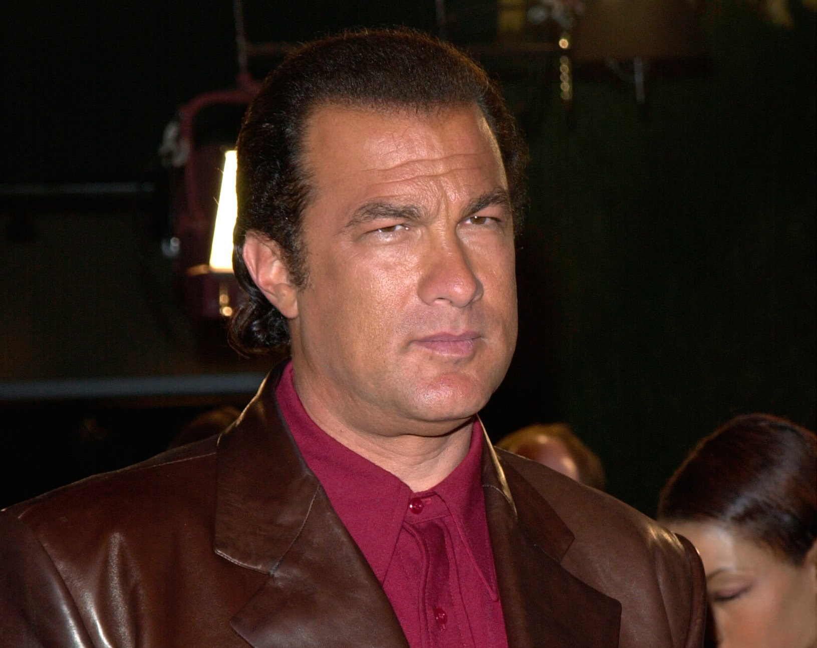 Steven Seagal wearing red shirt and brown jacket is looking at side - 2001