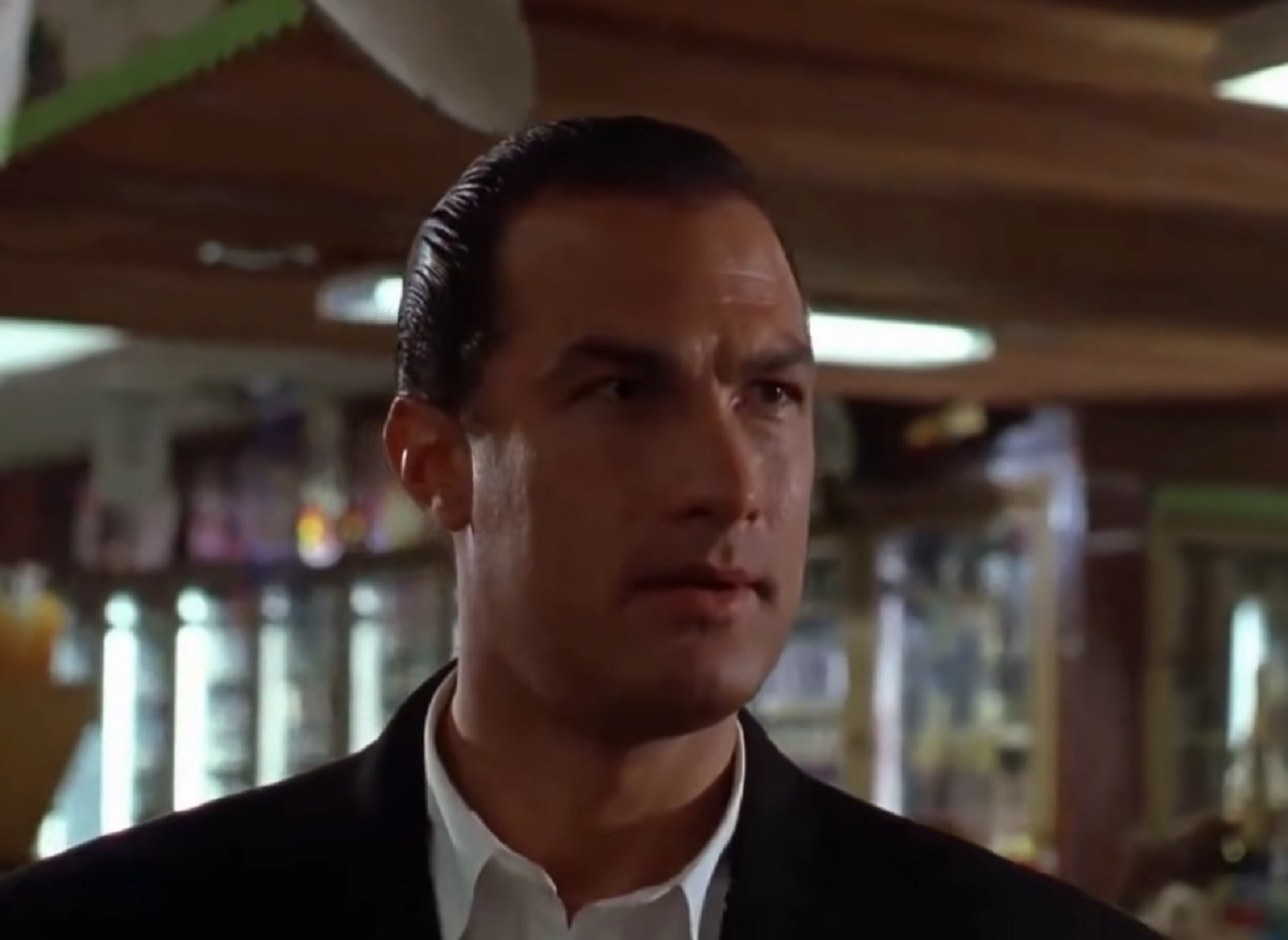 Screenshot: Steven Seagal wearing white shirt and black jacket is looking at side - from Hard To Kill (1990)
