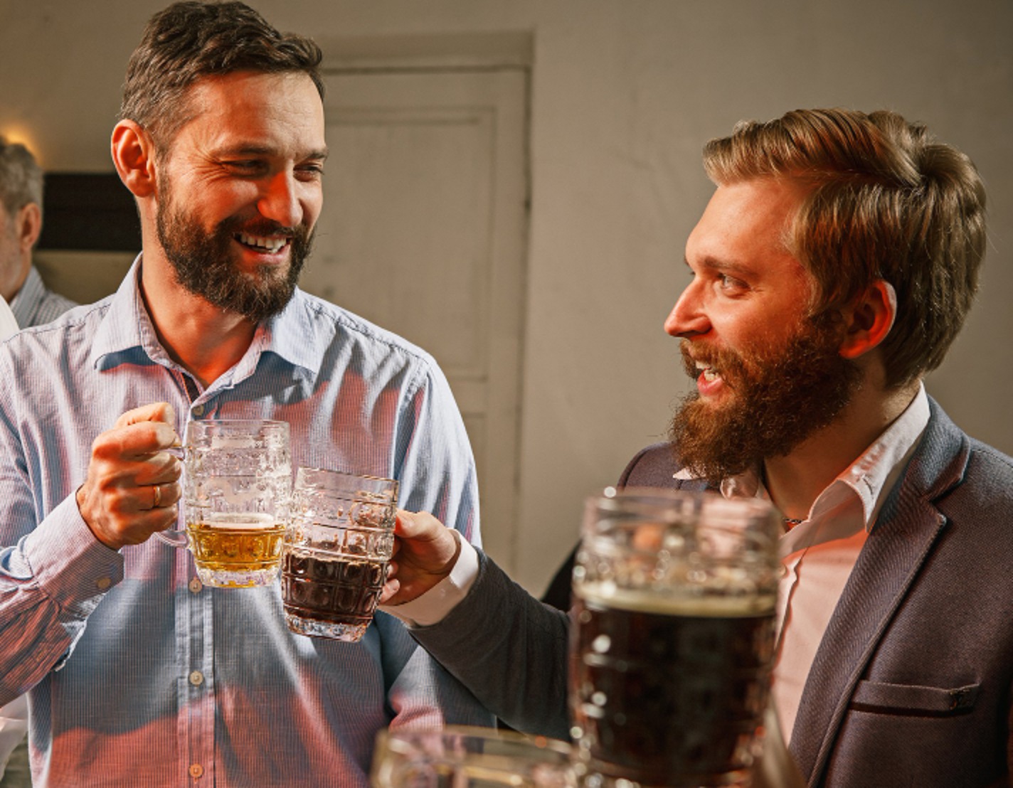 Bearded man laughing and making a toast with other man at party.