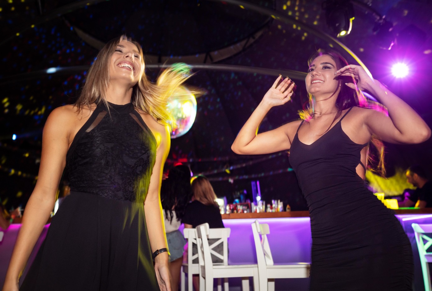 Two woman wearing black dresses are dancing at dance floor.