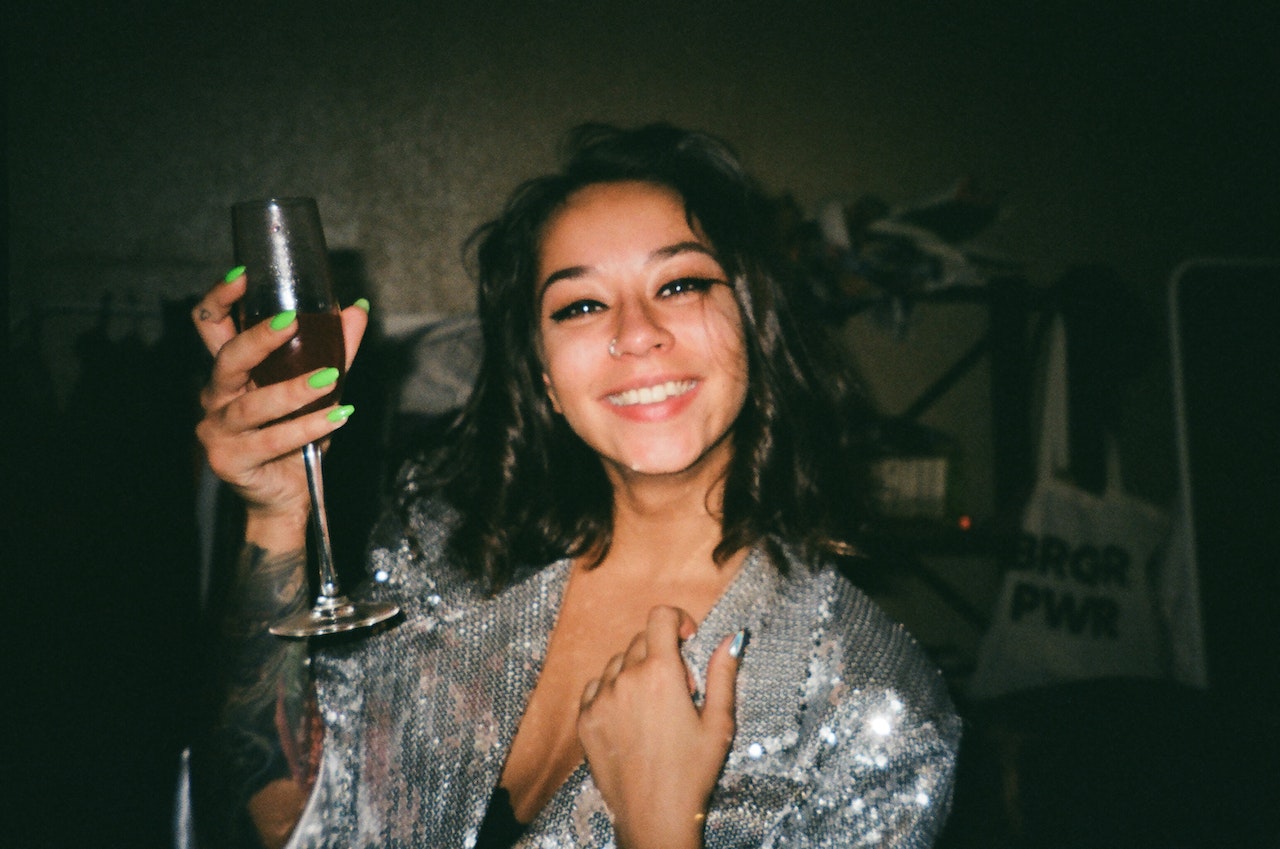Young woman is holding a glass and smiling at camera.