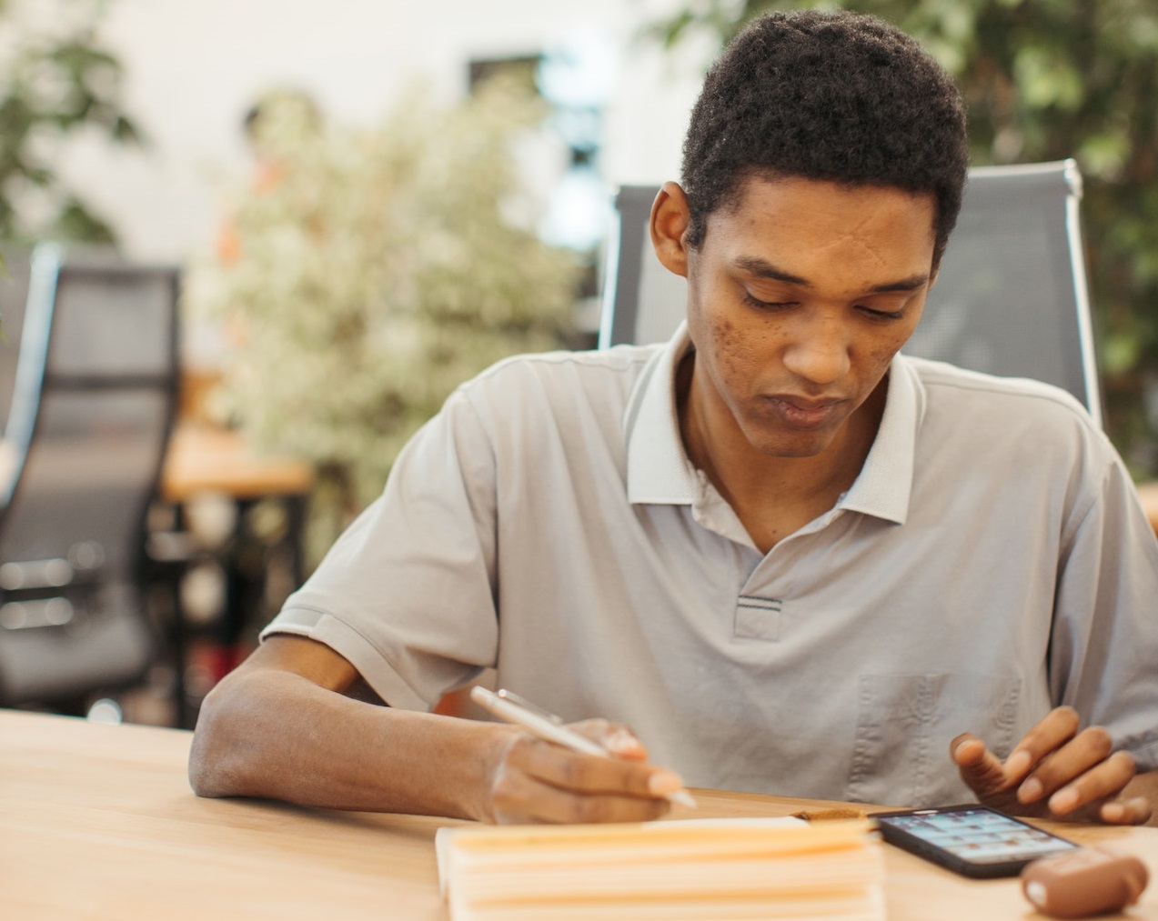 Young black man is looking at phone and writing something.