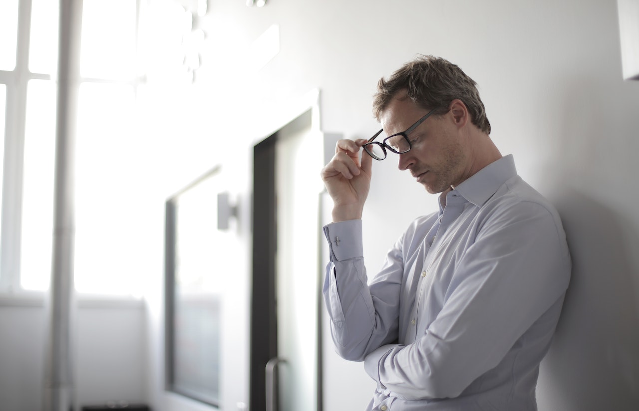 Man holding his glasses is standing next to a door.