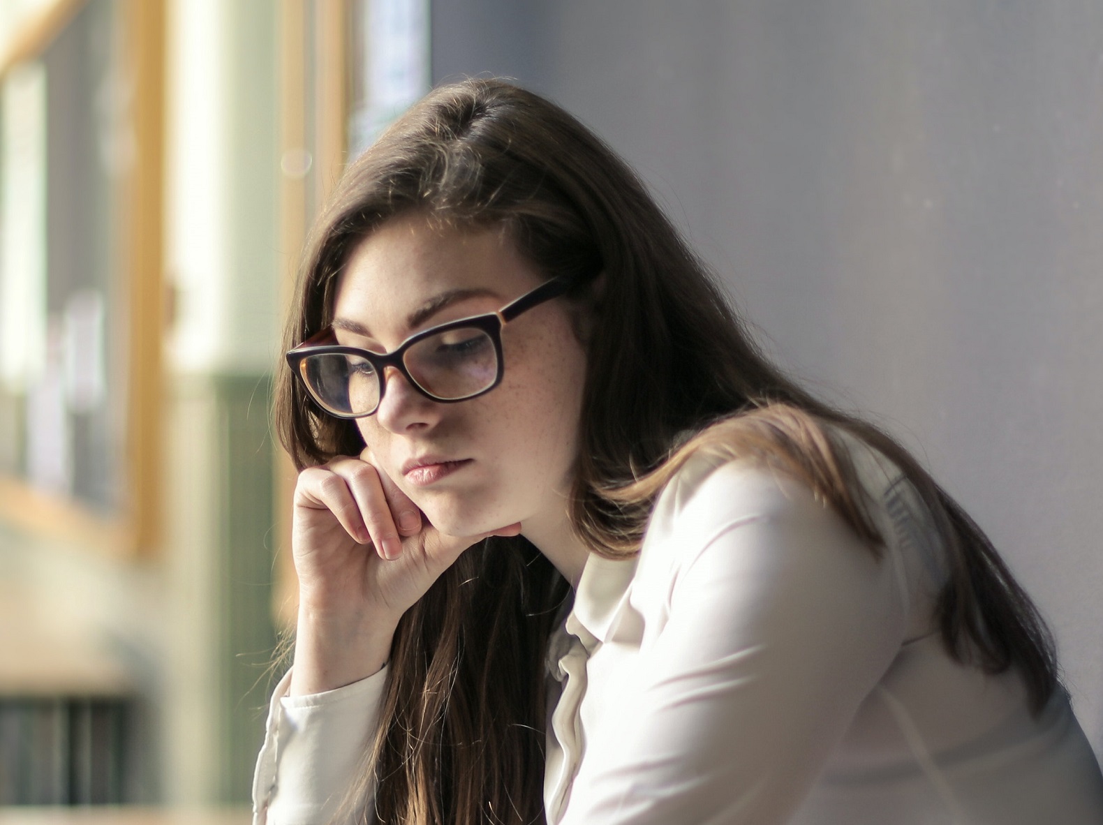 Sad young woman wearing white shirt is looking down.