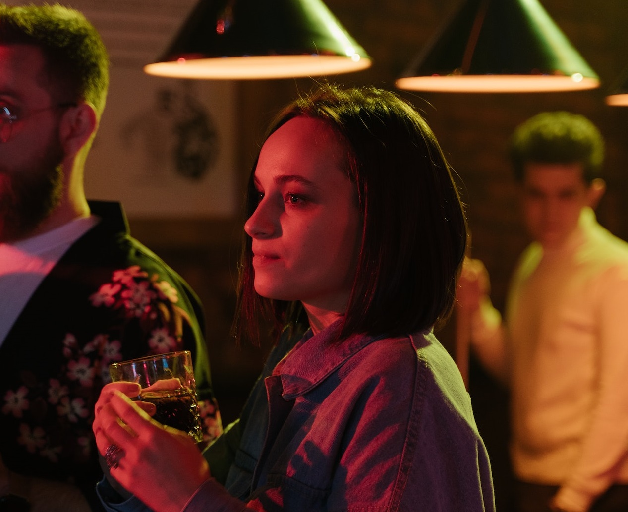 Sad woman holding glass is looking at others at party.