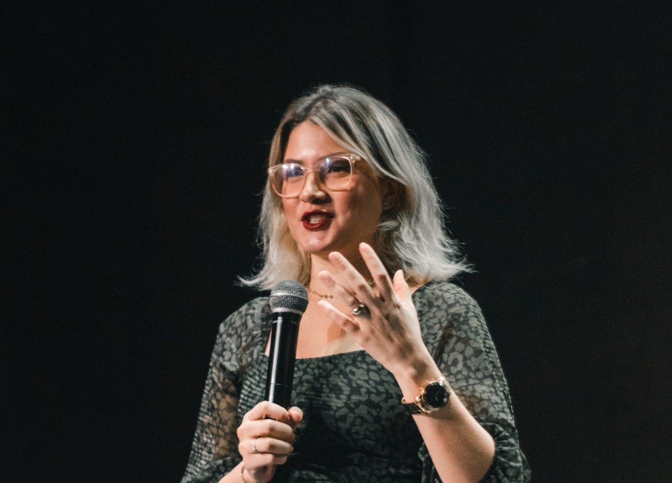 Young woman wearing grey dress is talking on microphone.