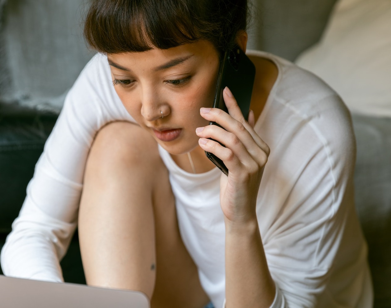 Young woman is talking on the phone and looking at her laptop.