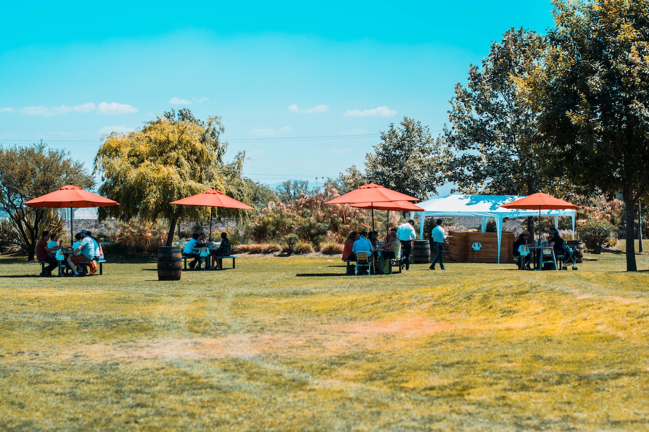 People having a picnic outside ,seating under a red umbrella.