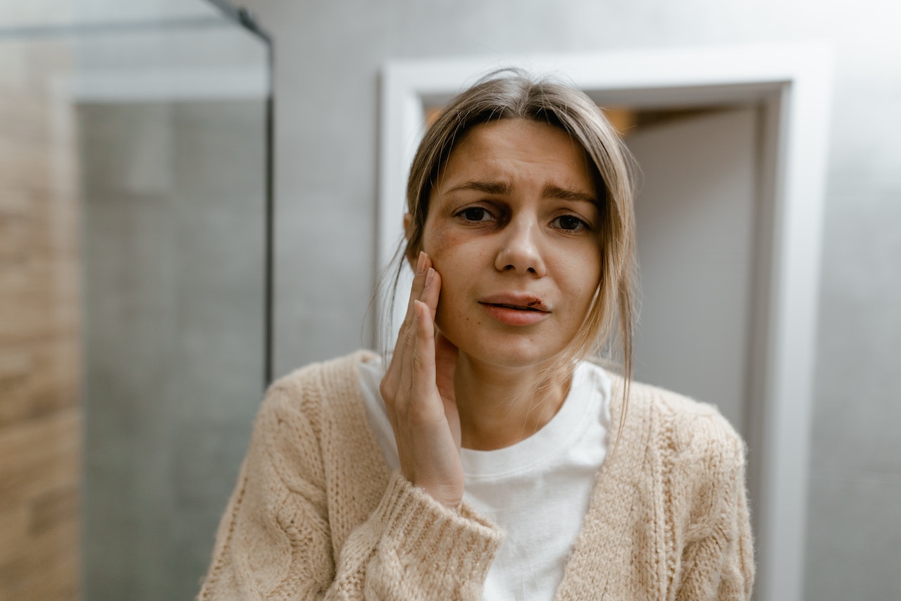 Woman is looking her bruised face on the mirror.