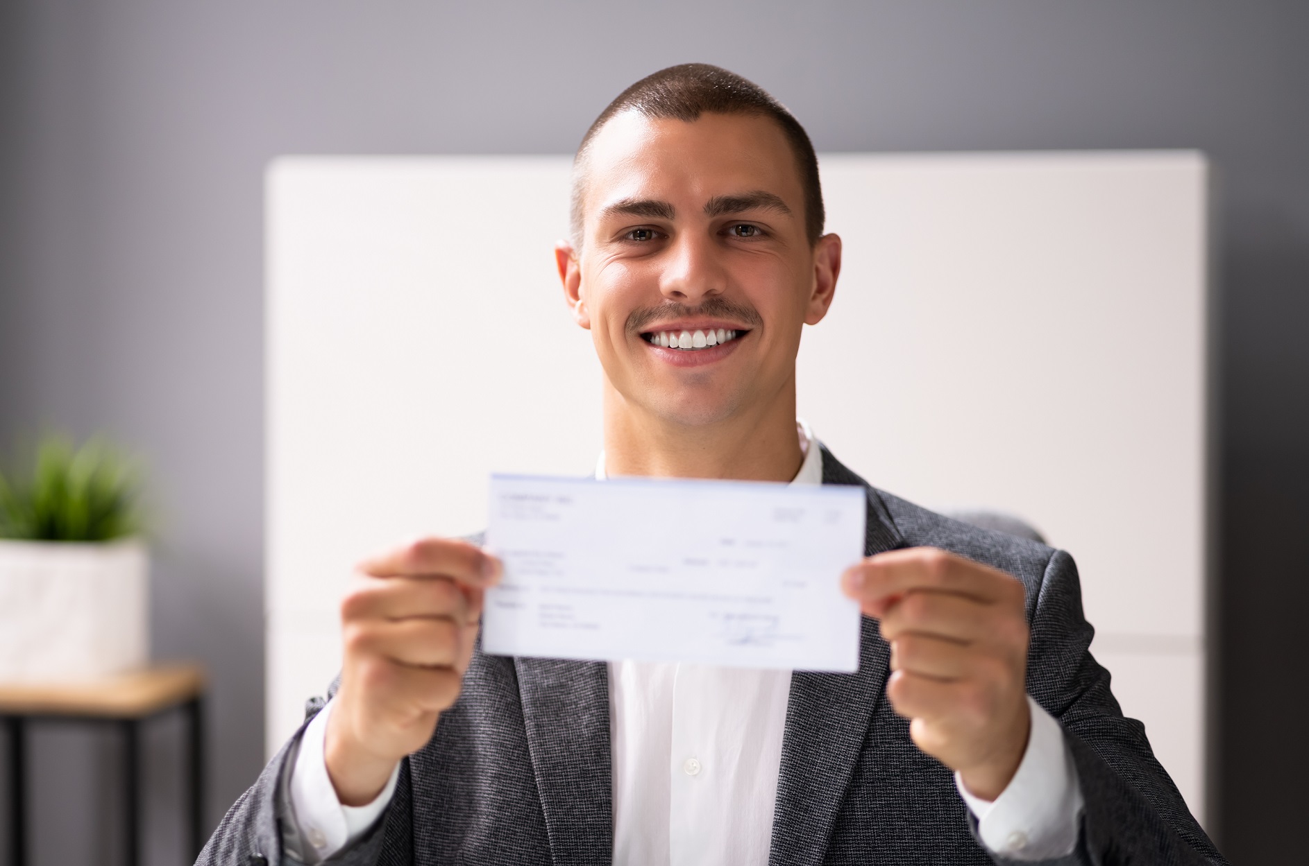 Man is holding a pay check in his hands and smiling at camera.