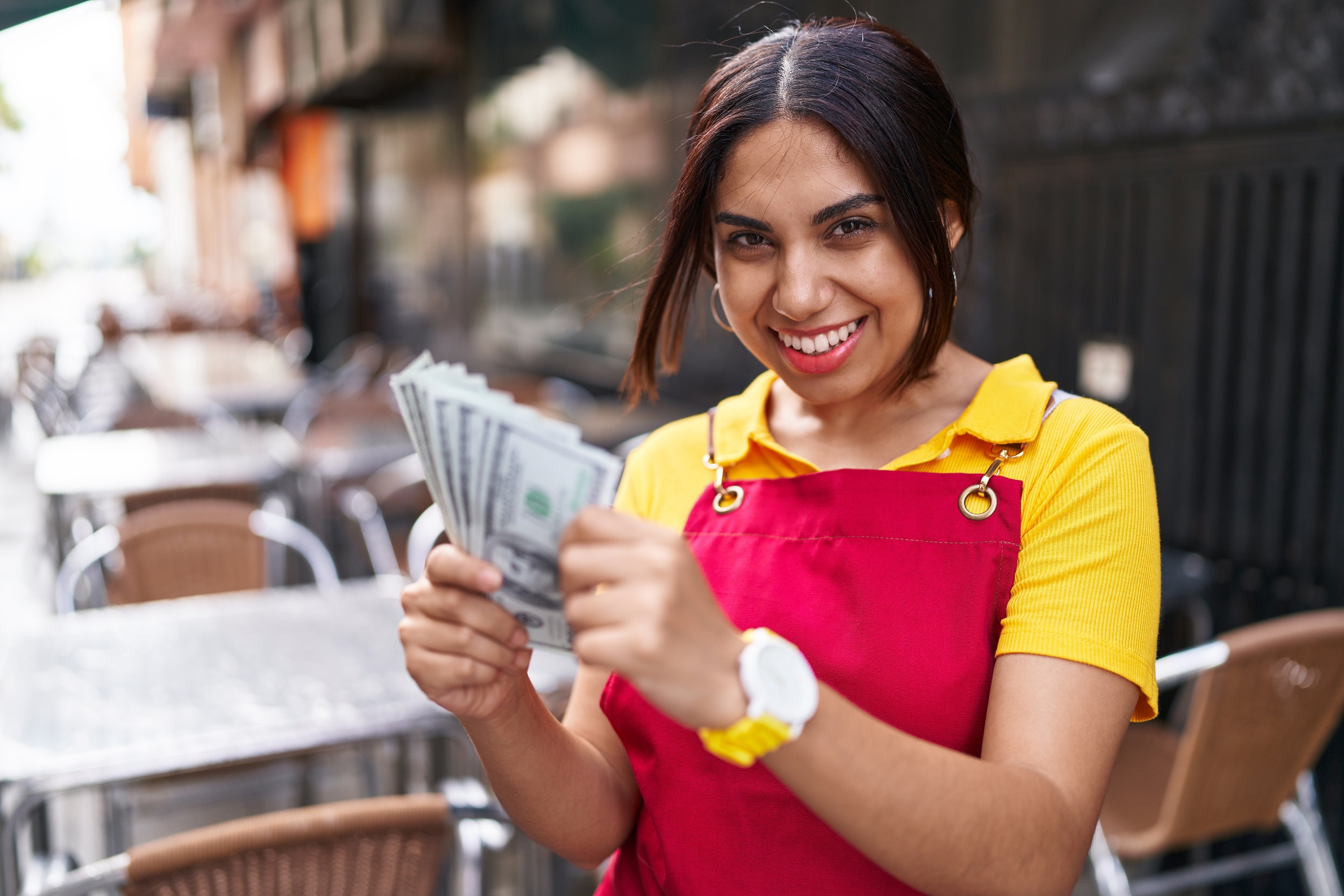 Young happy waitress is smiling and holding money at coffee shop.