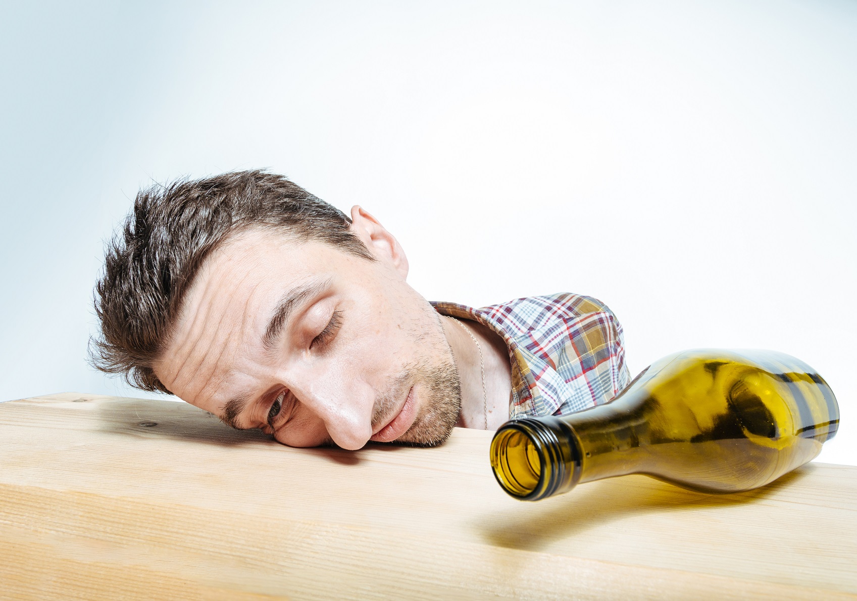 Drunk man is sleeping on the table with empty bottle next to him.