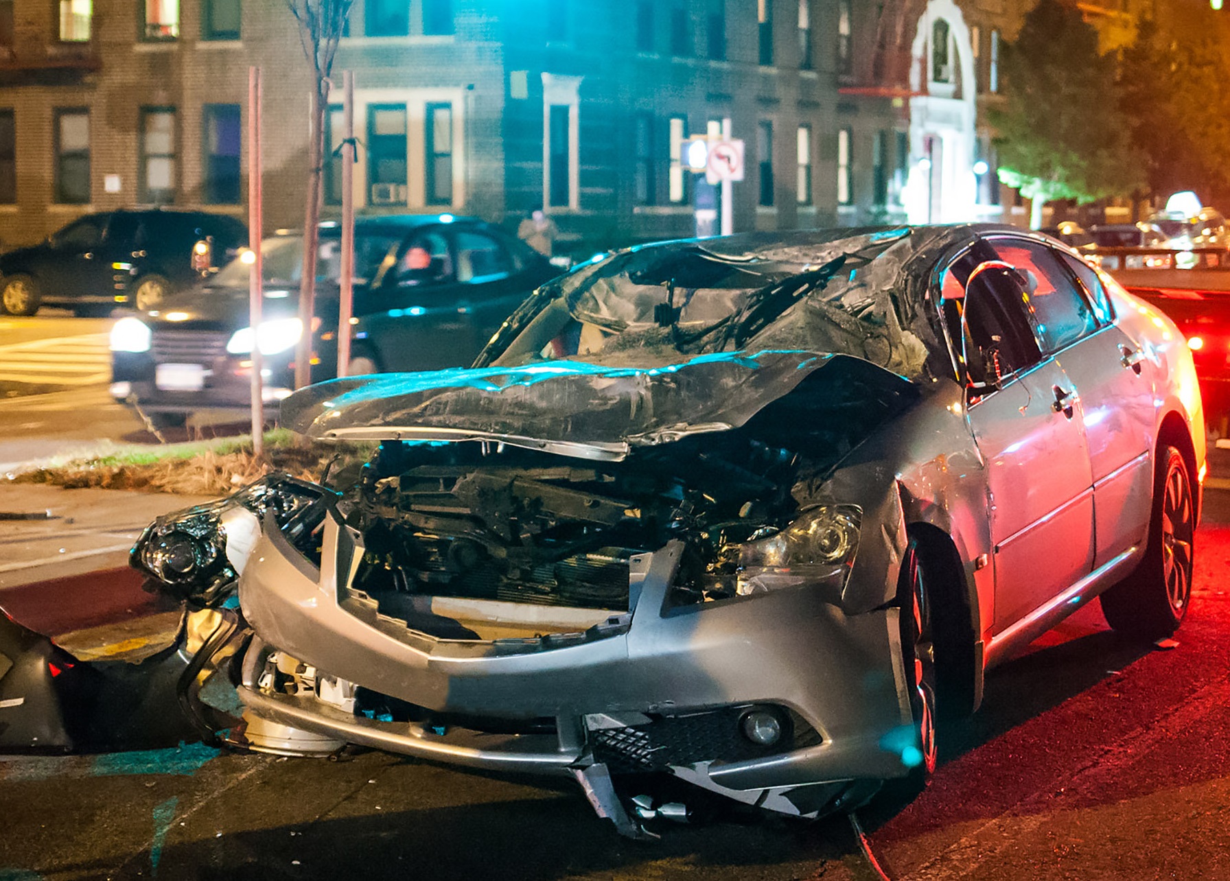 Destroyed silver car is standing on the road at night.