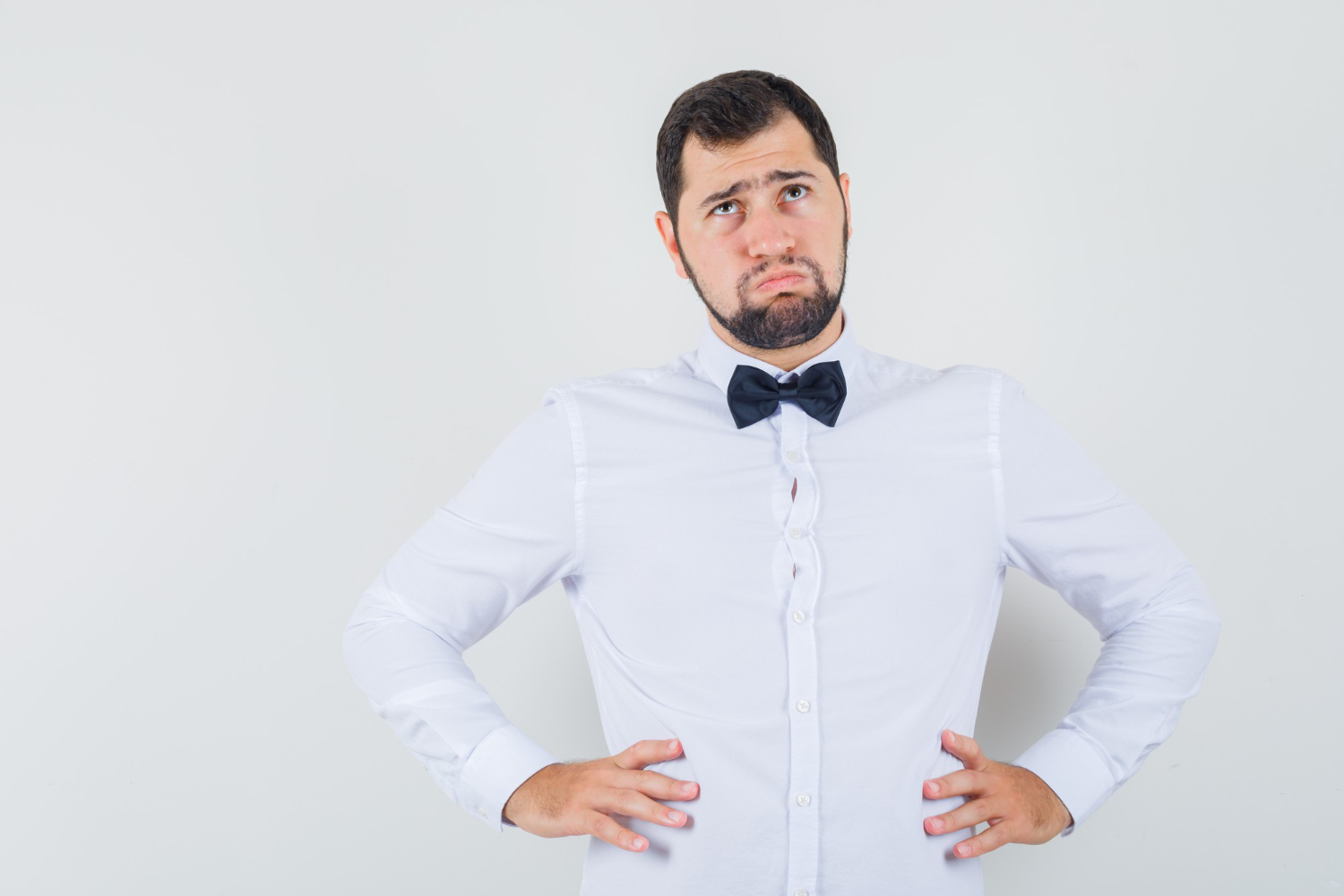 Young male waiter is looking up with sad face on grey background.