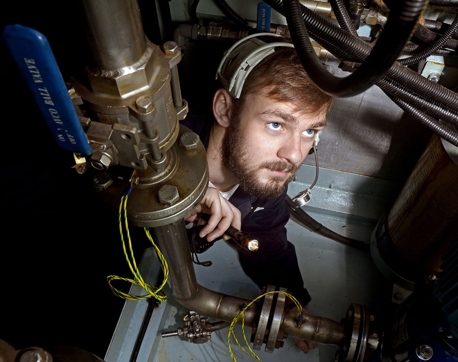 Marine Engineer at work in boat looking up wearing headphones.