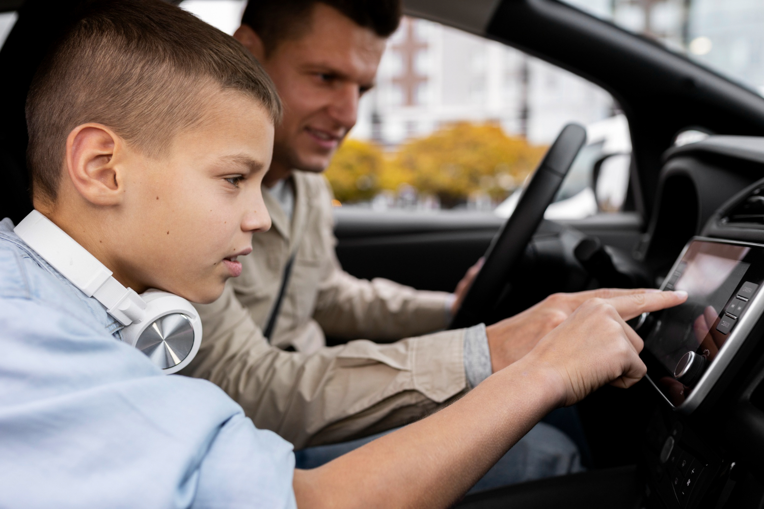 Young father is seating inside of a car with his small kid and smiling.