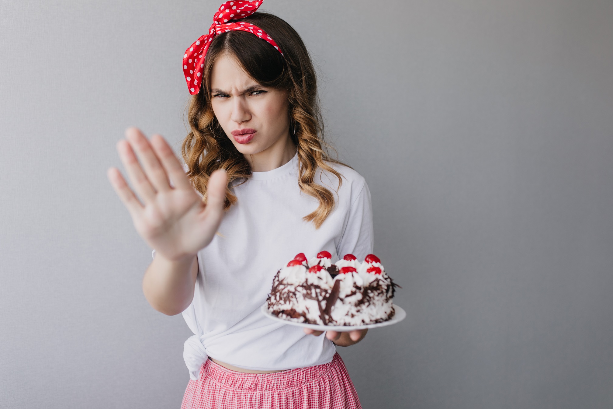 Young woman is holding a cake and making stop with her hand.