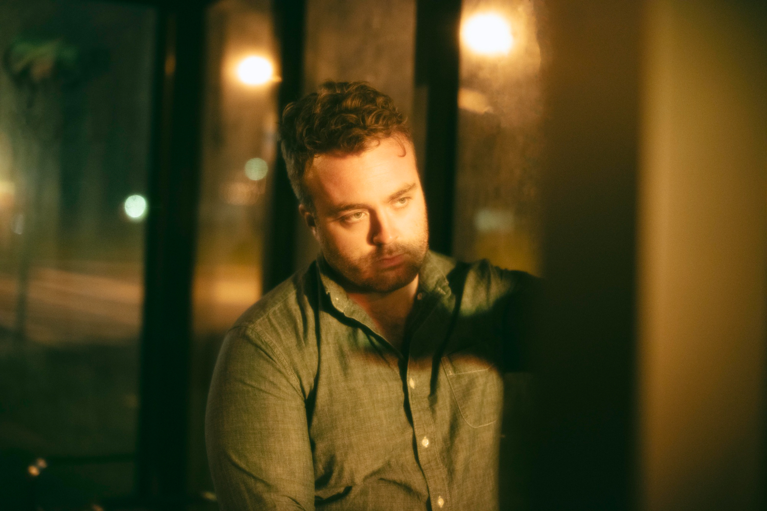 Man is looking upset thru the window at night.