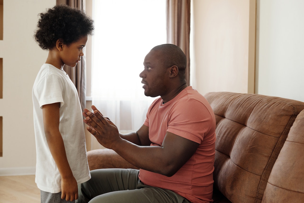 Young man seating on the sofa is talking with his small son and looking surprised.