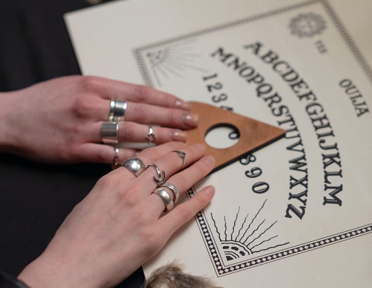 Hands of a women holding an arrow on a Ouija board game.