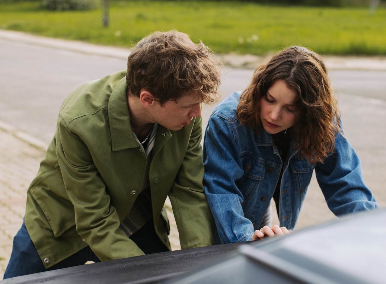 Man and woman are pushing a car outside of the road.