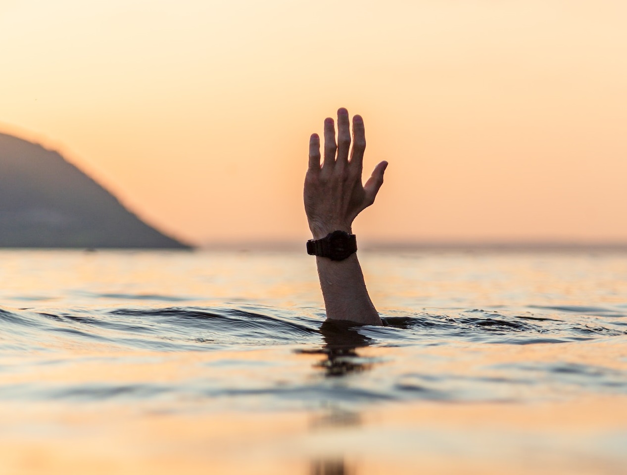 Hand out of the water of man drowning at sunset.