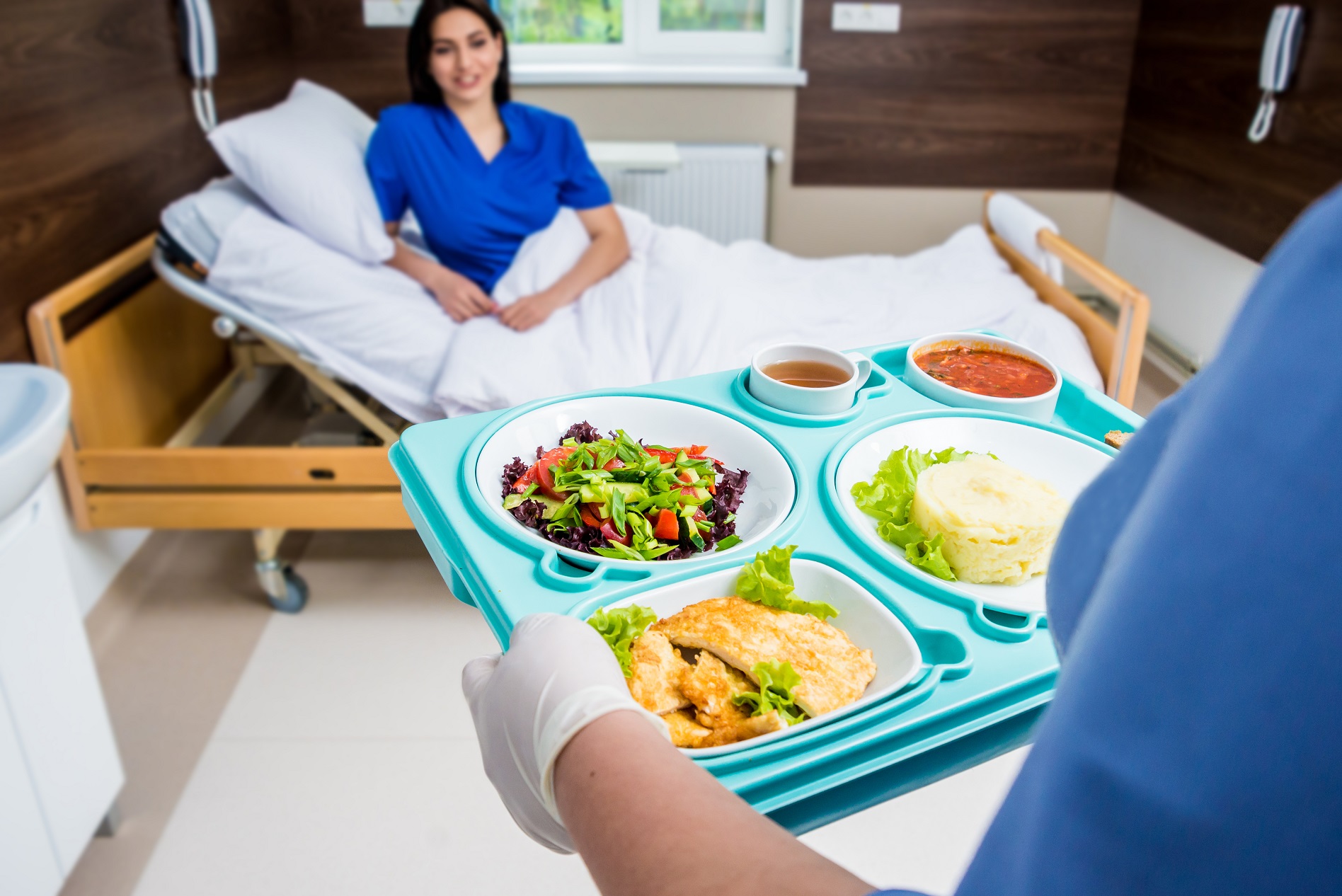 Nurse is holding a tray with breakfast for the young female patient.