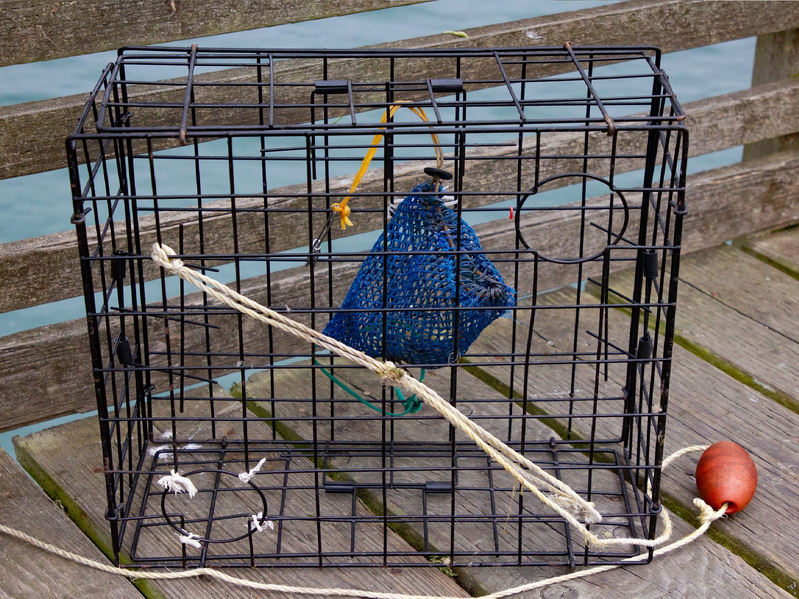 An empty crab trap cage is standing on the wooden boards.