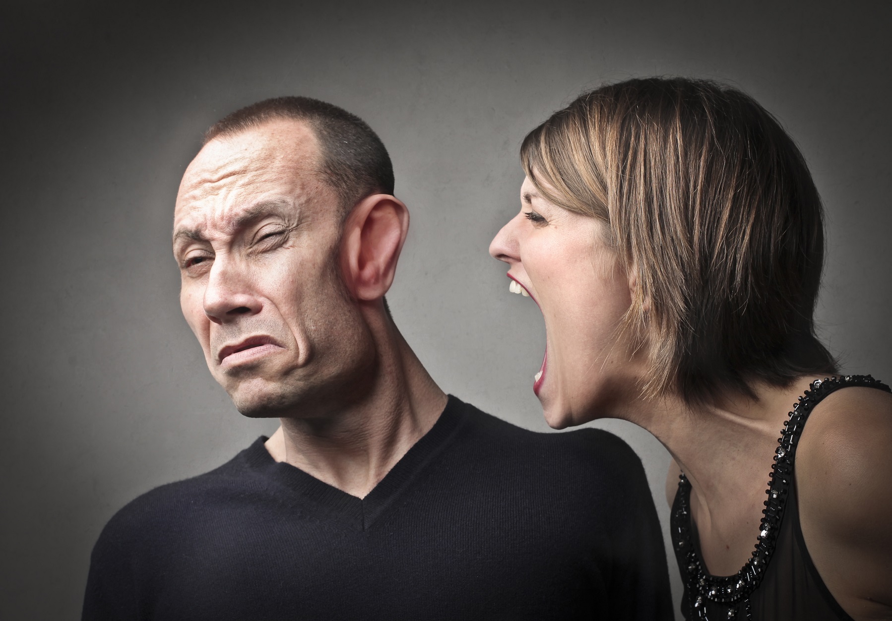 Angry woman screaming against her husband with his face deformed by the power of the scream