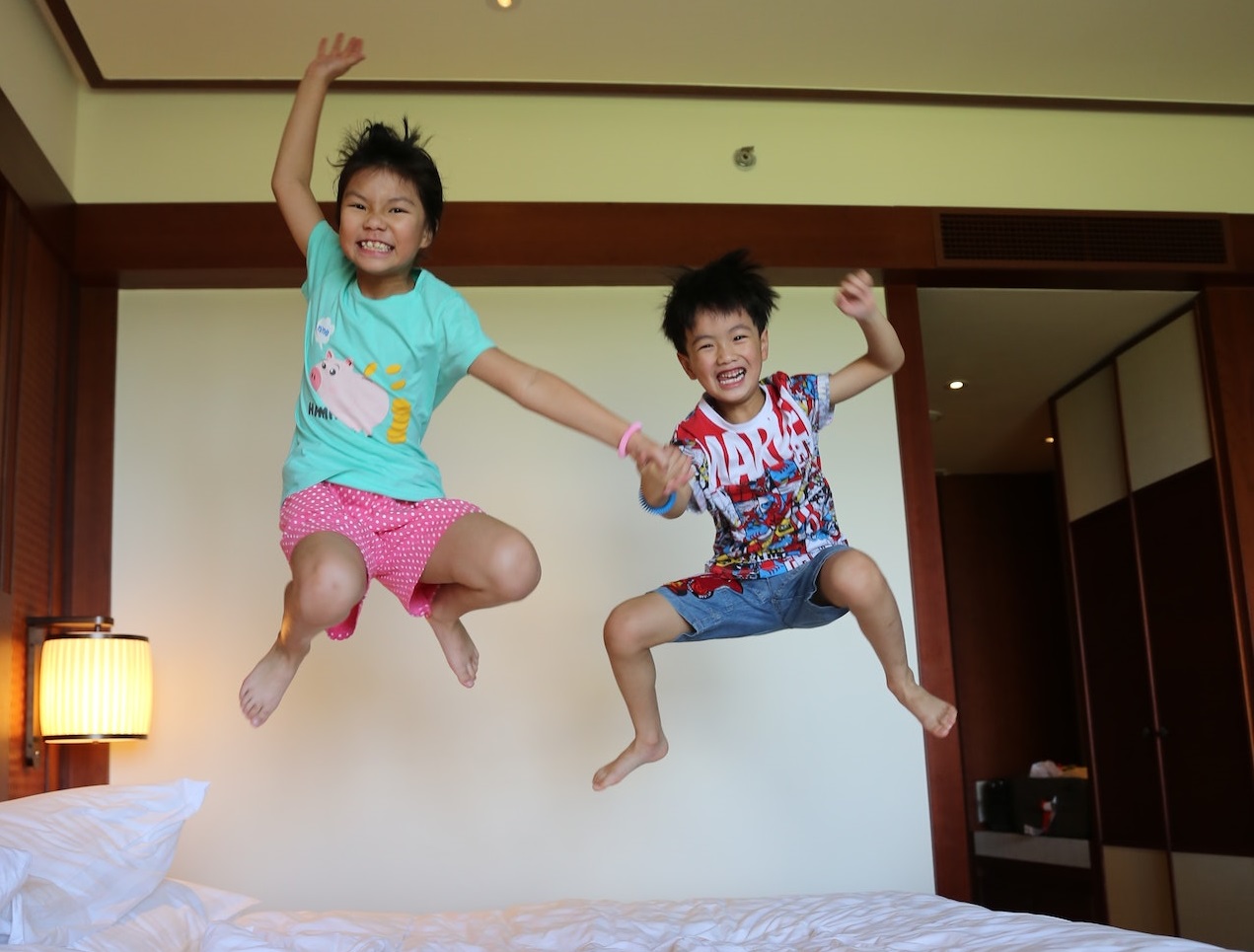 Two small kids are jumping on the bed in bedroom.