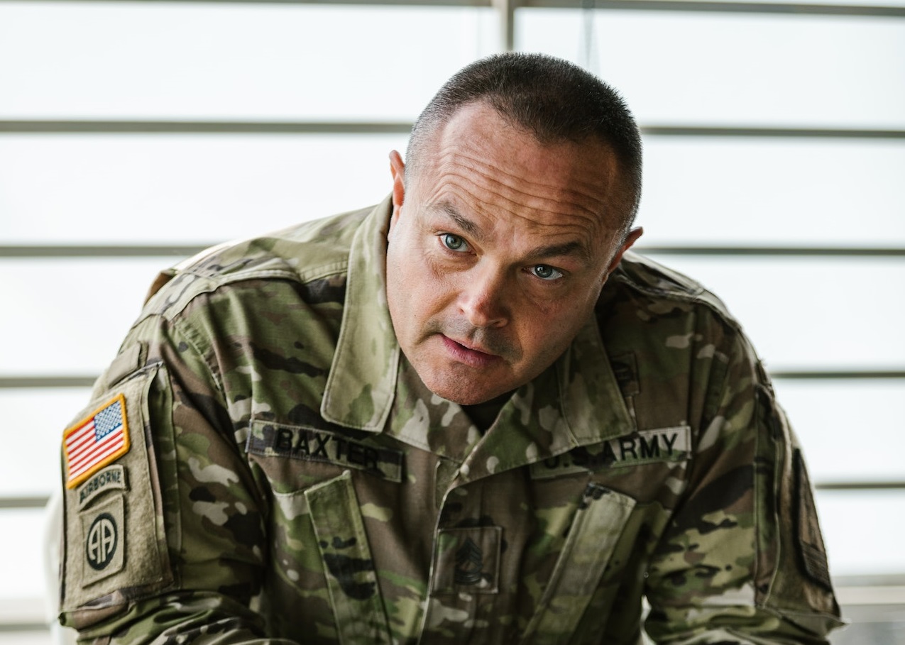 Man wearing military uniform is seating and looking at side.