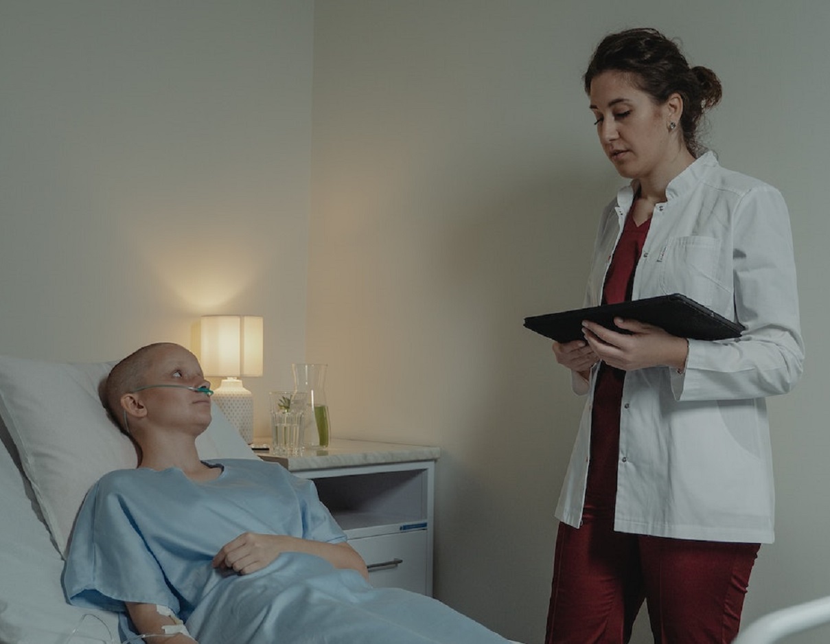 Sick female patient laying at hospital bed is talking with female doctor standing by her side.