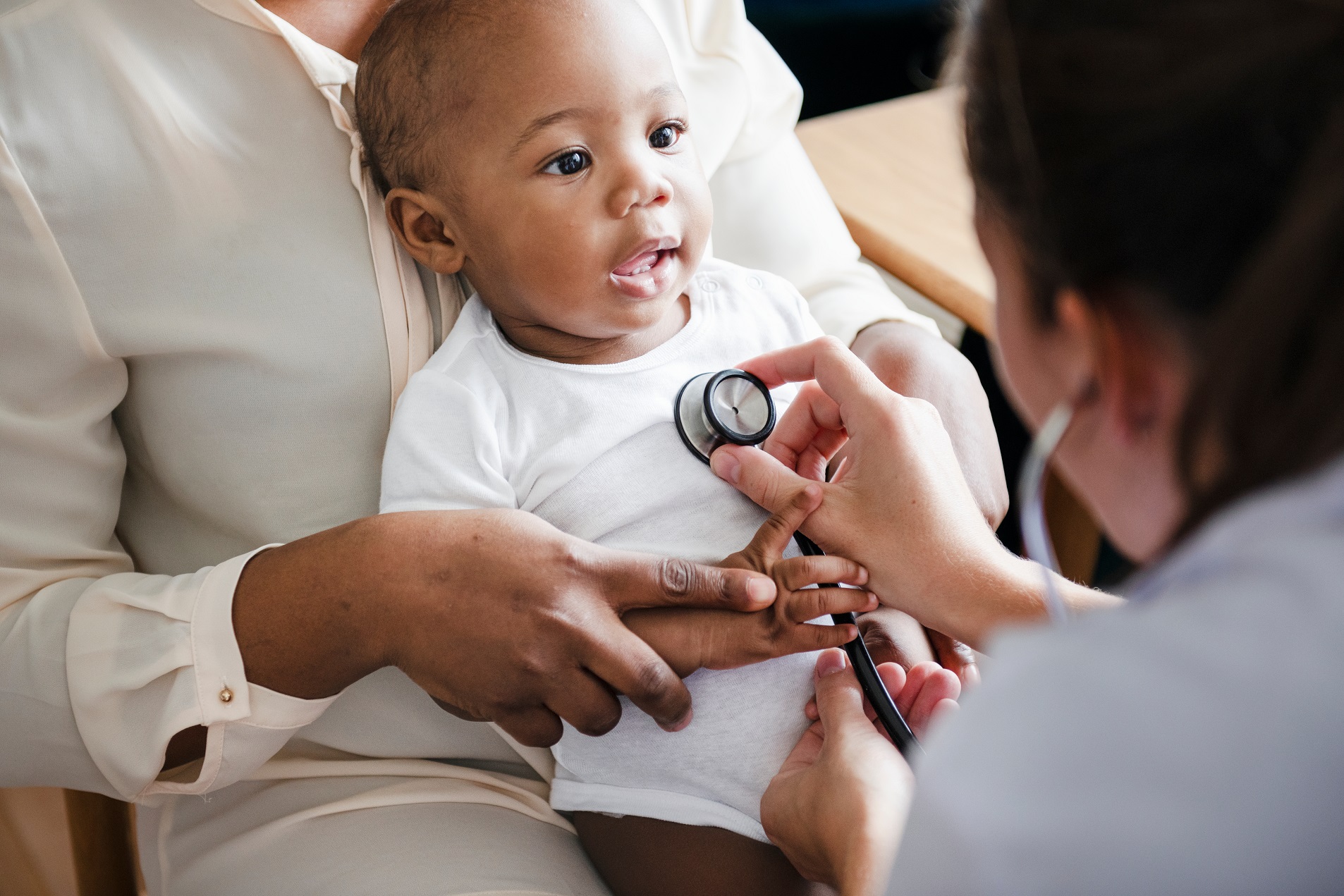 Female doctor is check in small baby wearing white clothes.