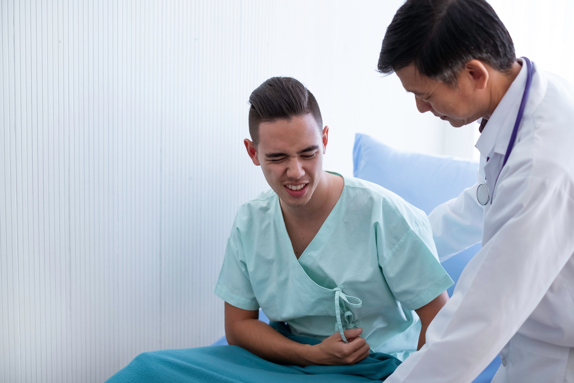 Male patient is talking with doctor and holding his stomach at hospital.