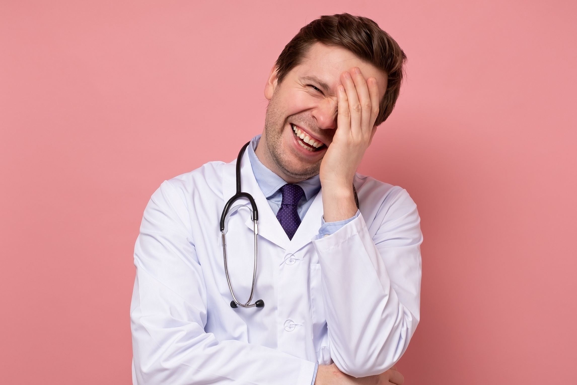 Young doctor is laughing at camera on red background.
