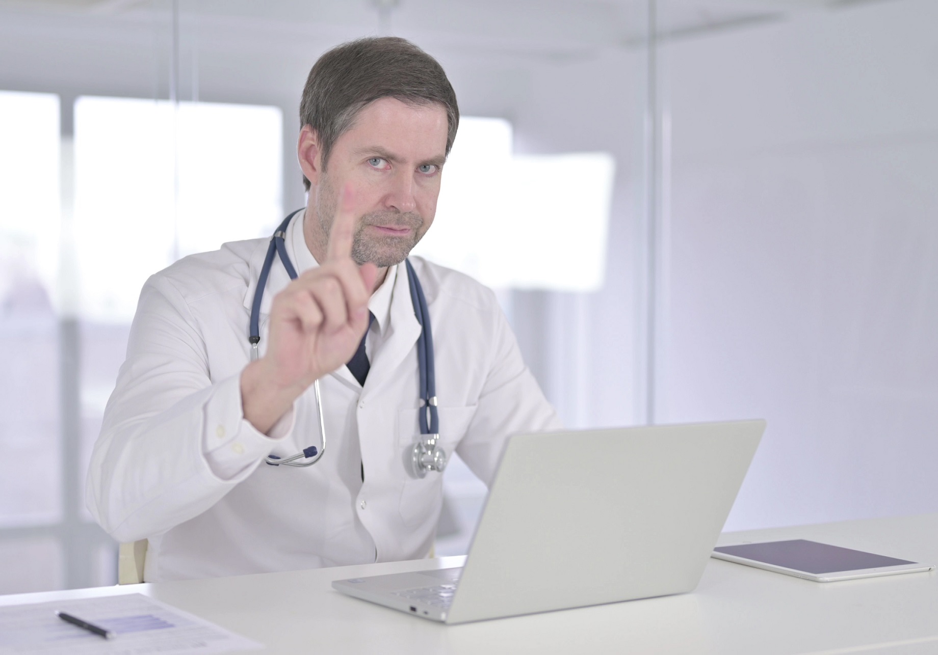 Male doctor is looking at camera and make NO hand gesture.