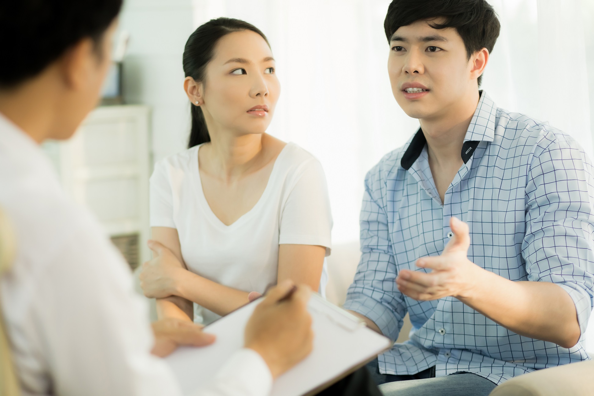 Young man is seating next to his wife and talking with a doctor at hospital.
