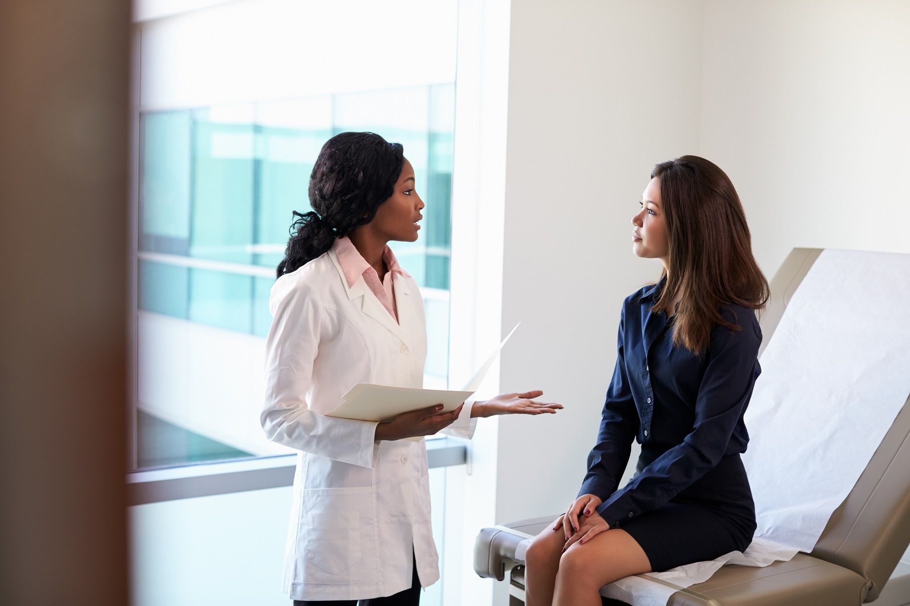 Female patient is talking with a female doctor standing next to her.