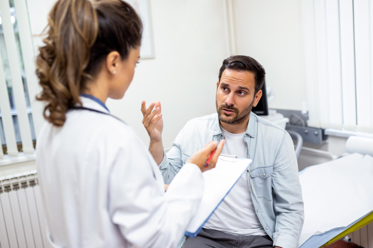 Male patient is talking with female doctor at her office.