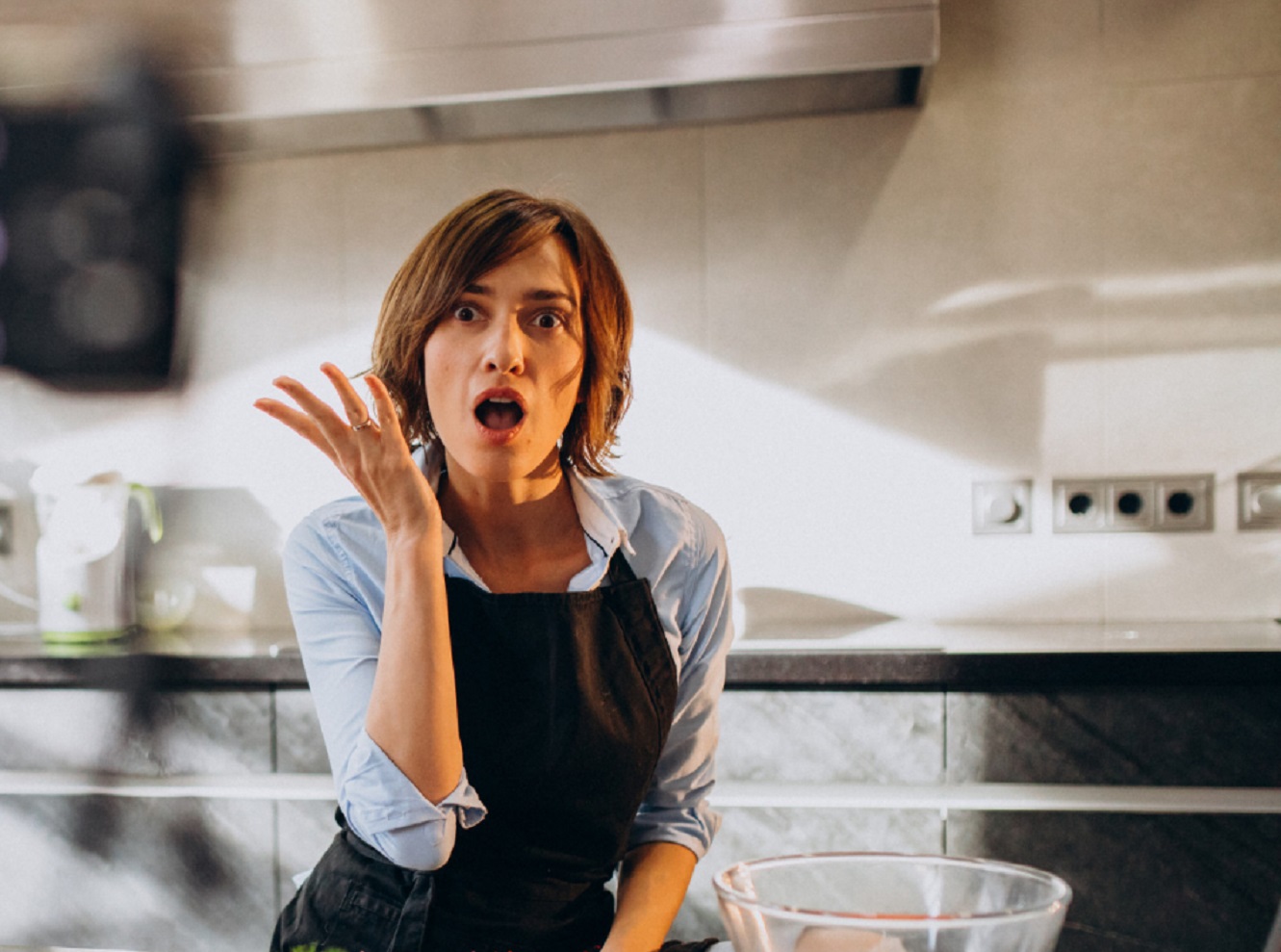 Woman is looking surprised at kitchen, making a hand gesture.