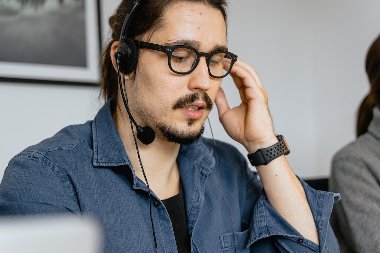 Young man with headphones is making a call on his desk.