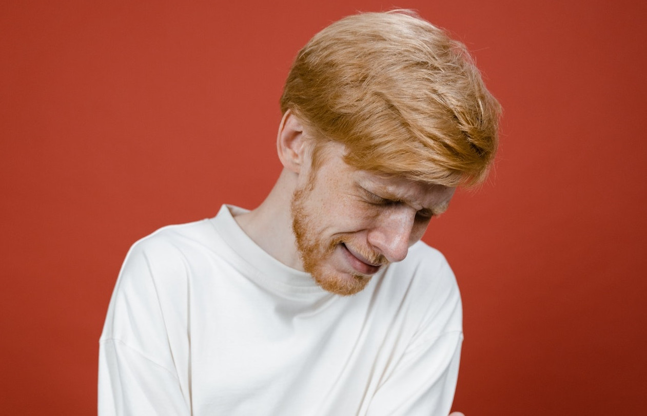 Sad man wearing white shirt is crying and looking down.