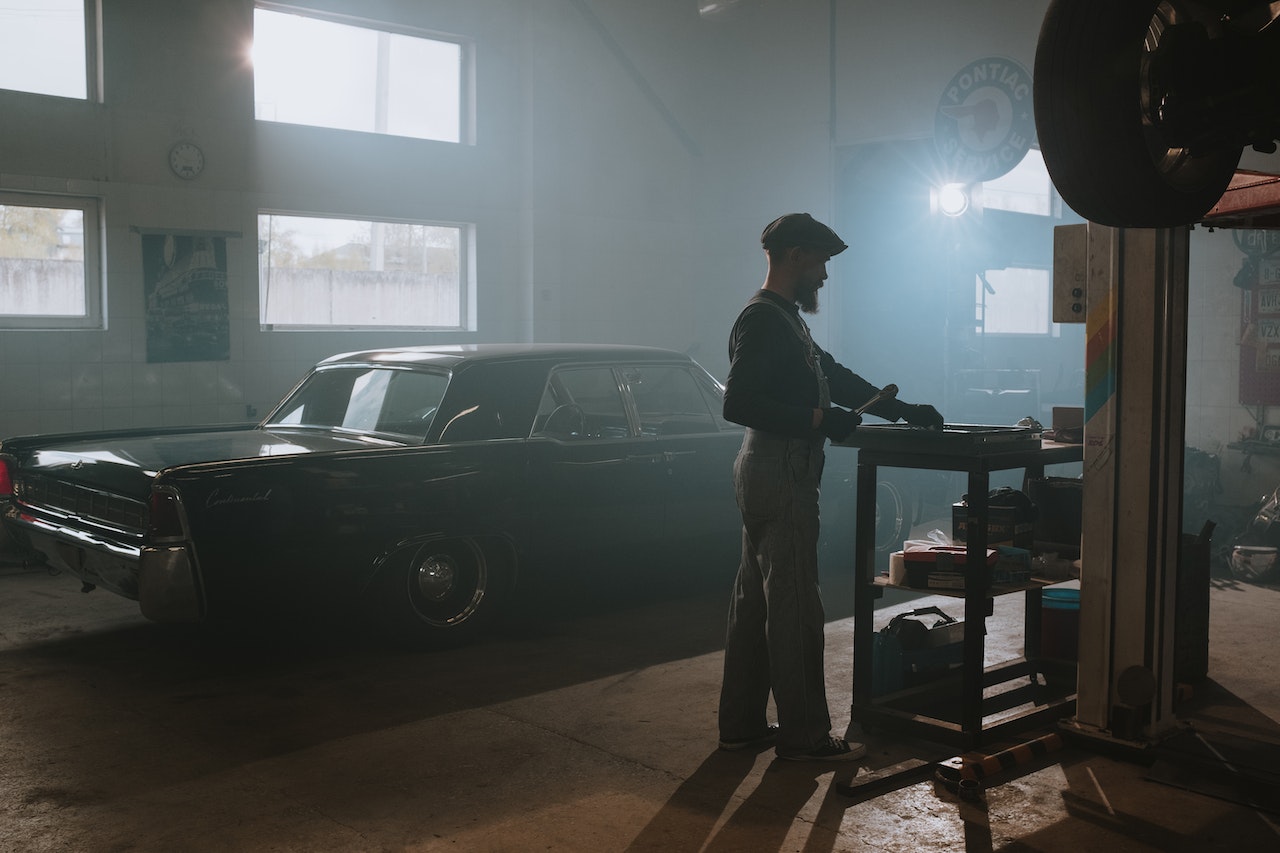 Mechanic is working next to a black car in workshop.