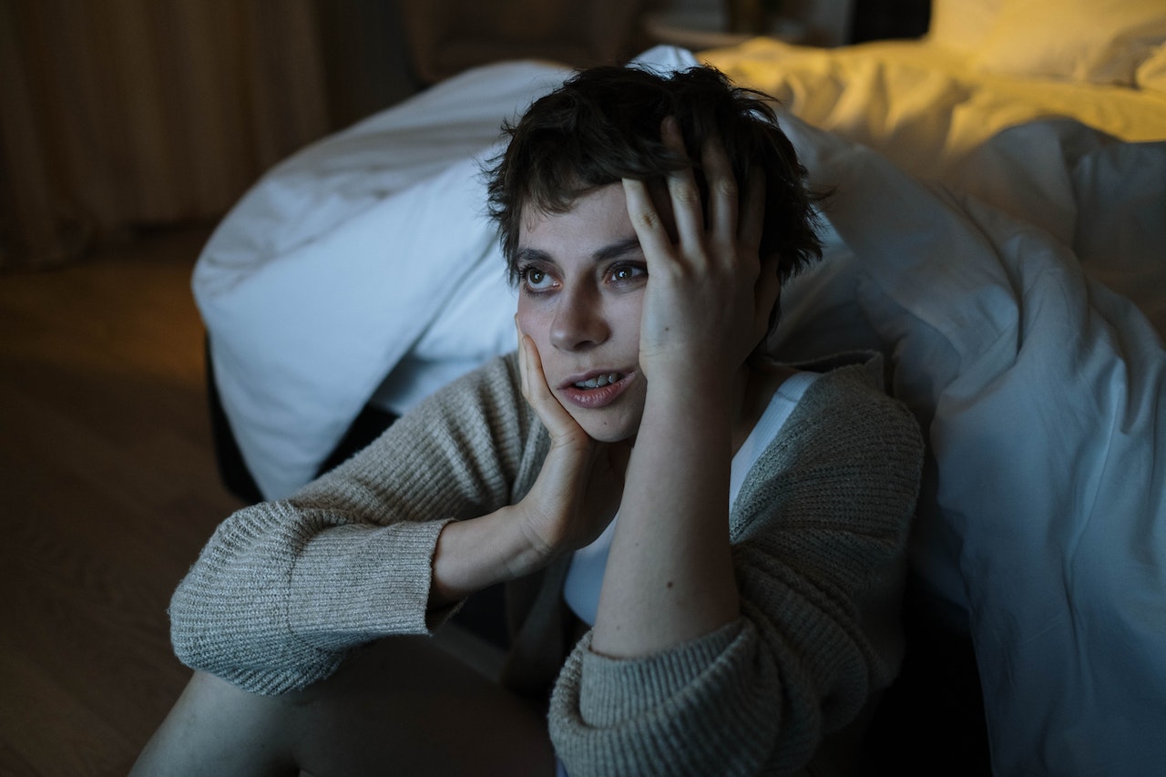 Scared woman is seating next to bed with upset face.