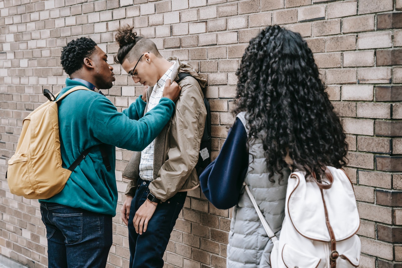 Two young man are arguing outside and young girl is watching.