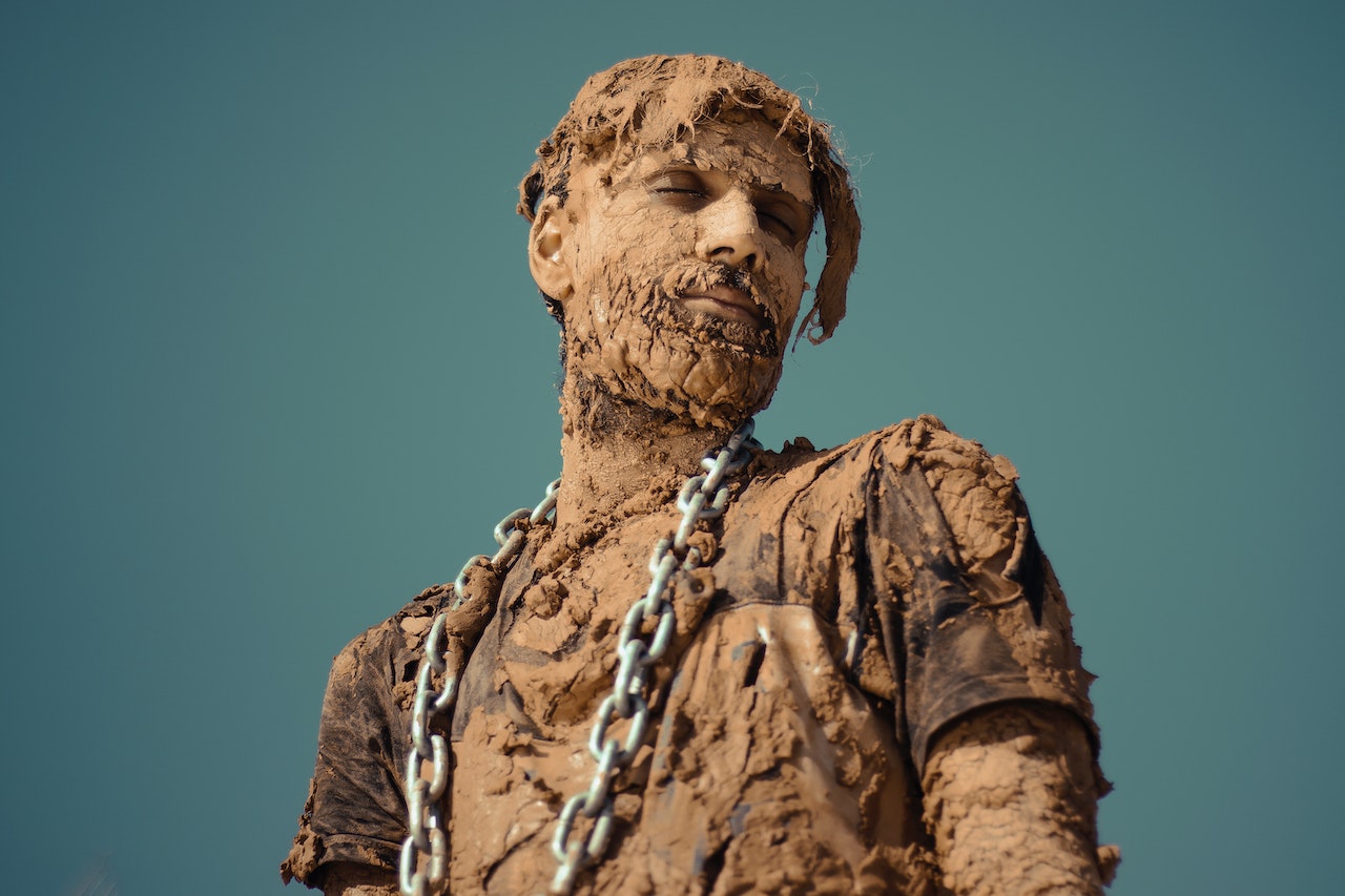 Man covered in dirt is wearing a chain and standing with closed eyes.