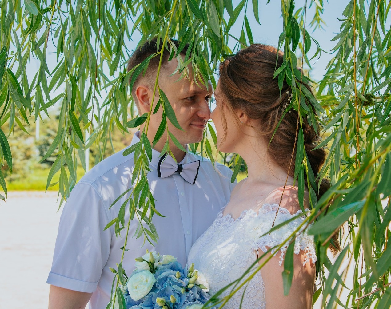 Happy couple are standing under the willow tree.