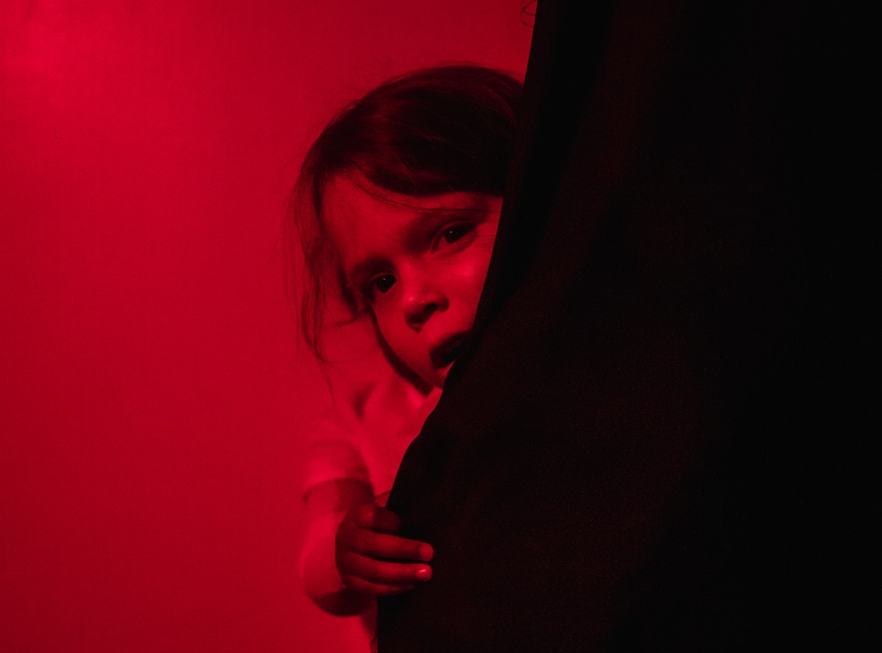 Small girl is hiding in red lighted room.